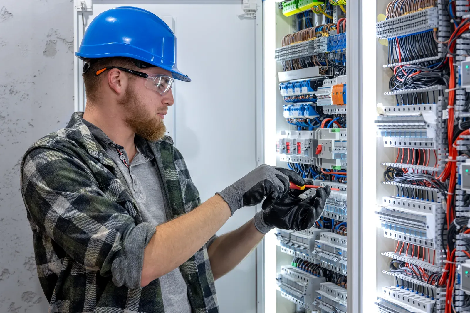 Electrician in a blue hard hat working inside a distribution board